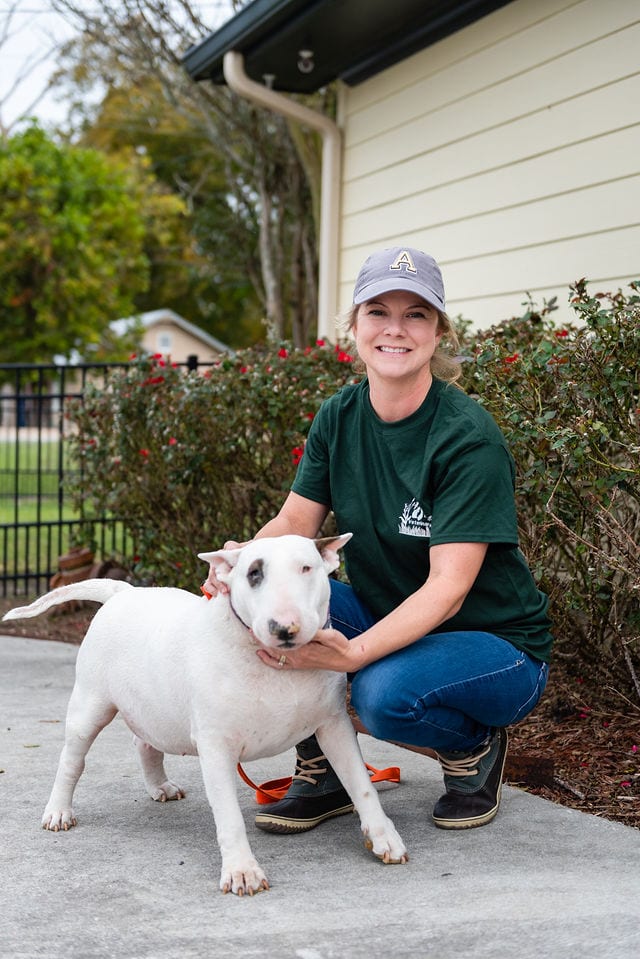 A woman kneeling down next to a dog.