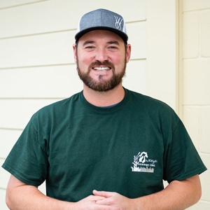 A man in a green shirt and hat standing next to a wall.