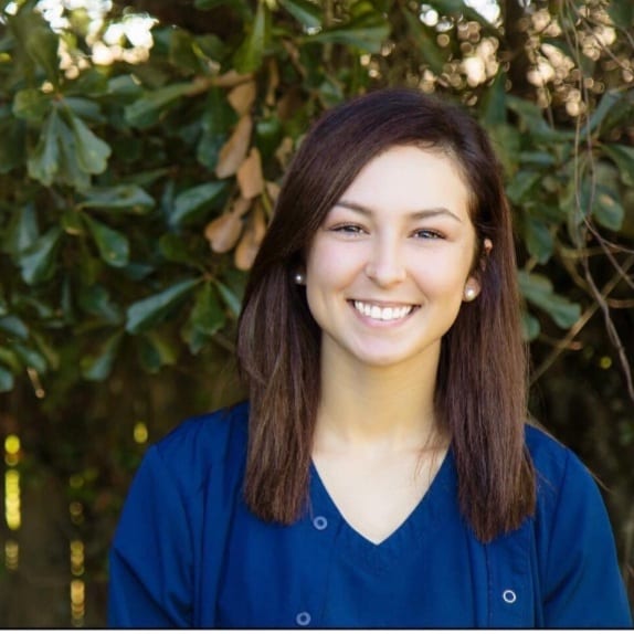 A woman smiling for the camera in front of trees.