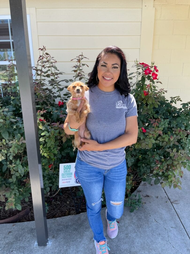 A woman holding her dog in front of some bushes